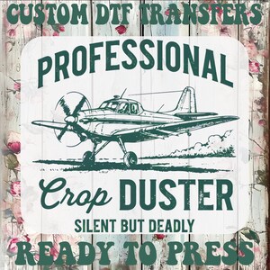 May include: A green and white graphic featuring a crop duster airplane. The text reads "PROFESSIONAL CROP DUSTER SILENT BUT DEADLY READY TO PRESS" and "CUSTOM DTF TRANSFERS" in a decorative font. The background is a floral and wood grain pattern.