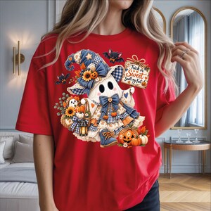May include: A red t-shirt featuring a graphic of a ghost wearing a blue plaid hat and dress, holding a sign that reads Trick or Sweet Smell my Feet. The design includes pumpkins, sunflowers, a lantern, and small bats on a light background.