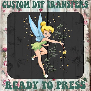 May include: A DTF transfer featuring Tinkerbell with the text "All You Need Is Faith, Trust, And Pixie Dust." The design includes a cartoon fairy with yellow hair, green dress, and blue wings, set against a black background with stars. The words "Custom DTF Transfers" and "Ready to Press" are also included.