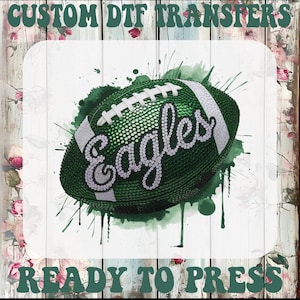May include: A green American football with the word "Eagles" in a sparkly font. The football has white stripes and laces. The words "CUSTOM DTF TRANSFERS" and "READY TO PRESS" are at the top and bottom of the image.