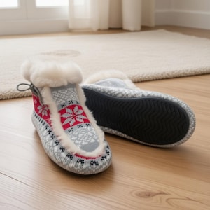 May include: A pair of gray and red knit slippers with a snowflake pattern and faux fur trim. The slippers have a rubber sole and a loop at the back. The slippers are designed for indoor use.