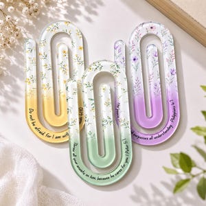 May include: Three large, U-shaped acrylic paperclips featuring floral patterns and printed text. One is yellow with yellow flowers, one is green with yellow flowers, and one is purple with purple flowers. Each displays a unique religious verse.