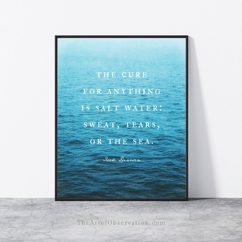 May include: A framed print with a blue ocean background and a quote in white text that reads: "The cure for anything is salt water: sweat, tears, or the sea." The quote is attributed to Isak Dinesen.