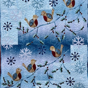 May include: A quilted wall hanging featuring a winter scene with six birds perched on a branch with holly and red berries. The background is light blue with snowflakes. The birds have brown, red, and blue details.