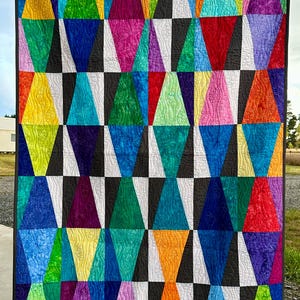 May include: A colourful quilt with a geometric pattern of triangles in various shades of blue, green, purple, yellow, orange, and red. The triangles are arranged in a repeating pattern on a black and white chequered background.
