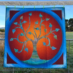 May include: A quilted wall hanging featuring a stylised tree with blue leaves against a red and orange background. The tree is surrounded by a blue circle with a red border.