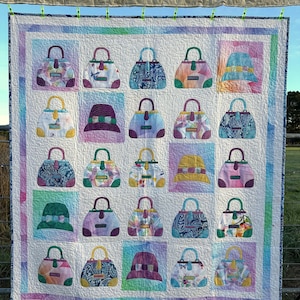 May include: A white quilt with a patchwork design featuring various colorful handbags and hats. The quilt is made with a variety of fabrics and textures, and the handbags and hats are all different shapes and sizes. The quilt is hanging on a clothesline.