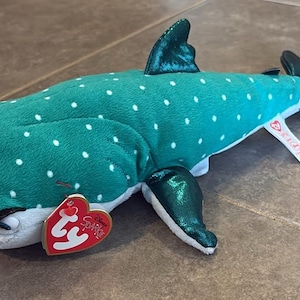 Peut inclure: Une peluche en forme de requin-baleine avec un corps sarcelle à pois blancs, un ventre blanc et des nageoires vert métallisé. Le jouet comporte une étiquette rouge en forme de cœur Ty Sparkle à l'avant et une étiquette en tissu blanc sur le côté.