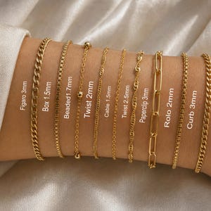 May include: A collection of nine gold-tone metal chains labeled with their specific styles and widths: Figaro 3mm, Box 1.5mm, Beaded 1.7mm, Twist 2mm, Cable 1.5mm, Twist 2.5mm, Paperclip 3mm, Rolo 2mm, and Curb 3mm, arranged in a parallel row.