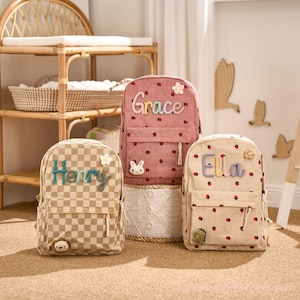 Peut inclure: Trois sacs à dos personnalisés pour enfants. L'un est rose à pois rouges avec le nom "Grace", un autre est beige à pois rouges avec le nom "Ella", et le troisième est à carreaux avec le nom "Henry". Chaque sac a un élément décoratif unique.
