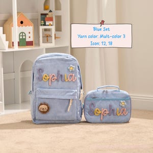 May include: A light blue corduroy backpack and matching lunch bag set. The backpack features the name "Sophia" in colorful embroidery, a flower applique, and a lion patch. The lunch bag also has the name "Sophia" embroidered.