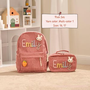 May include: Pink corduroy backpack and matching lunch bag set. The backpack features the name "Emily" in colorful embroidery, a bunny applique, and a carrot charm. The lunch bag also has the name "Emily" and a bunny applique.