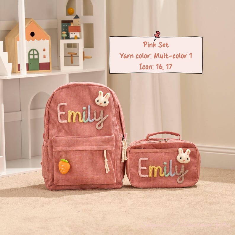 May include: Pink corduroy backpack and matching lunch bag set. The backpack features the name "Emily" in colorful embroidery, a bunny applique, and a carrot charm. The lunch bag also has the name "Emily" and a bunny applique.