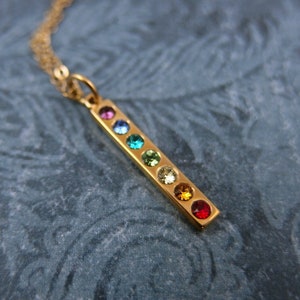 May include: A gold necklace with a pendant featuring a bar of rainbow-colored gemstones.