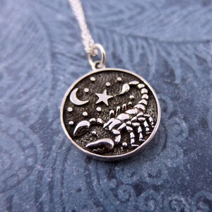 May include: Silver pendant necklace featuring a detailed scorpion design with a crescent moon and star on a starry background.