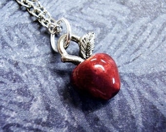May include: A silver chain necklace with a red apple charm. The apple has a silver stem and leaf.
