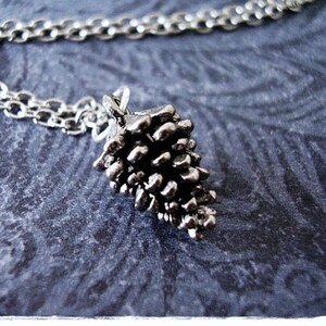 May include: A silver chain necklace with a silver pine cone pendant. The pine cone is detailed and realistic.