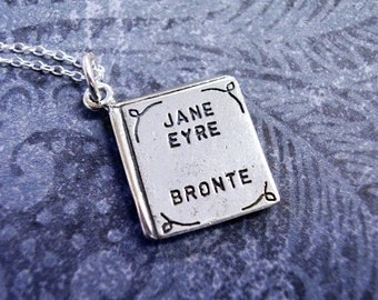 May include: Silver necklace with a charm shaped like a book. The charm has the title "Jane Eyre" by "Bronte" engraved on it.