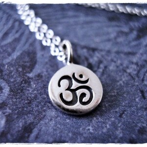 May include: A silver chain necklace with a silver pendant featuring the Om symbol.