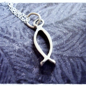 Puede incluir: Un collar de plata con un colgante de pescado simple y minimalista. El colgante es un contorno estilizado y hueco de un pez.