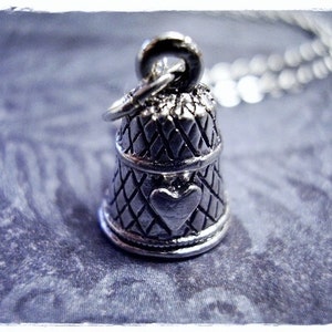 Peut inclure: Un charme de dé à coudre en argent avec un motif de cœur, attaché à une chaîne en argent.