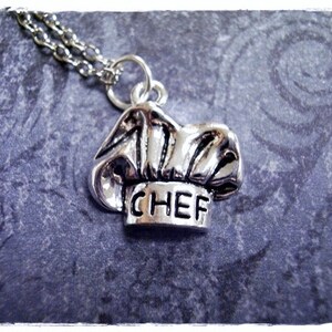 May include: Silver necklace with a chef hat charm. The charm has the word "CHEF" inscribed on it.