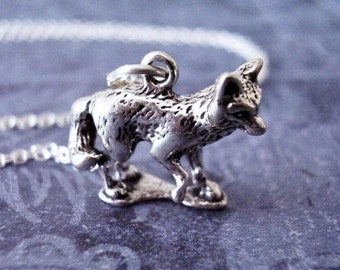 May include: A silver fox charm necklace with a detailed fox pendant. The fox is standing on all four paws with its tail curled behind it. The necklace is made of a silver chain.