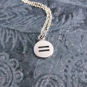 May include: A silver necklace with a round pendant featuring two parallel lines. The pendant is hanging on a silver chain.