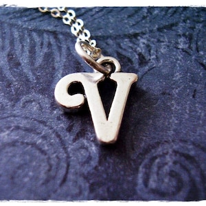 Puede incluir: Collar de plata con un dije en forma de letra V cursiva.
