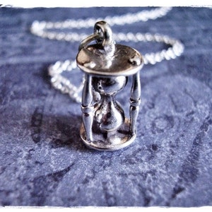 May include: A silver hourglass pendant necklace. The hourglass is detailed with a delicate design and hangs from a silver chain.