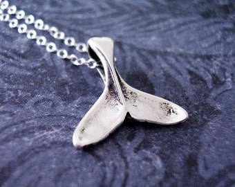 Può includere: Una collana d'argento con un ciondolo a forma di coda di balena. Il ciondolo è dettagliato e ha una finitura testurizzata.