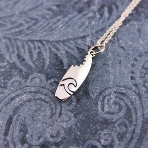 May include: Silver necklace with a surfboard pendant. The pendant has a wave design.