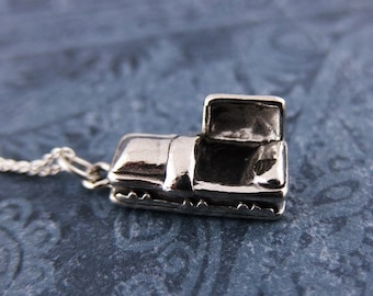 May include: A silver charm necklace featuring a small, open coffin pendant. The coffin is detailed with a hinged lid and a textured surface.