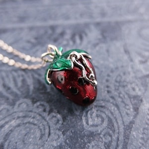 May include: A silver chain necklace with a red and black enamel strawberry charm. The strawberry has a green leaf and a silver stem.