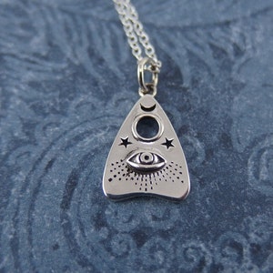 May include: A silver pendant necklace with a triangular charm featuring a crescent moon, a star, and an eye design. The charm is reminiscent of a Ouija board planchette.