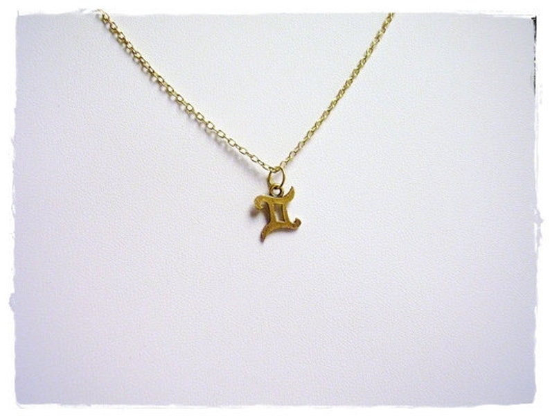 May include: A gold chain necklace with a gold pendant in the shape of the Gemini zodiac symbol.