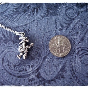 May include: A silver necklace with a charm of a witch riding a broomstick. The charm is about the size of a dime.