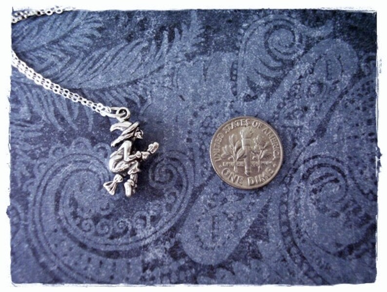 May include: A silver necklace with a charm of a witch riding a broomstick. The charm is about the size of a dime.