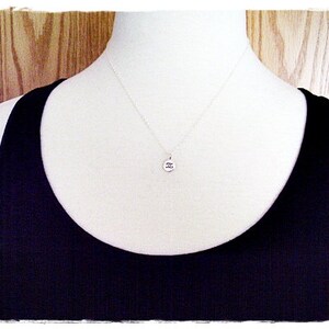 May include: A silver necklace with a small round pendant featuring the Roman numeral 'II'. The necklace is displayed on a white mannequin wearing a black tank top.