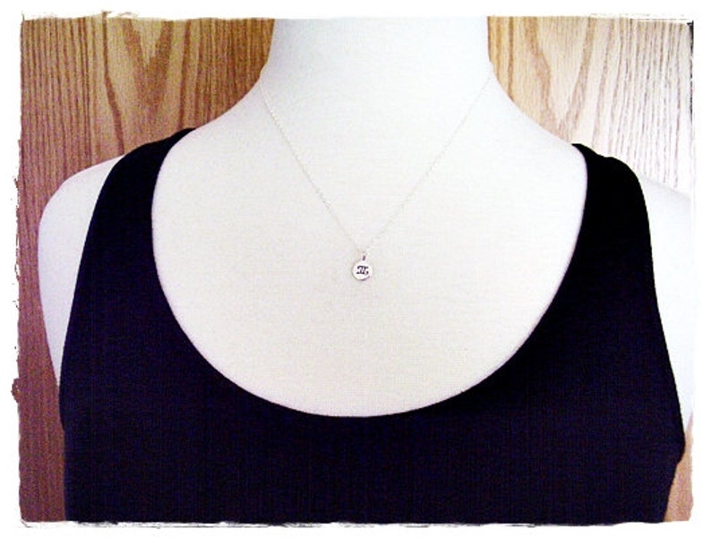 May include: A silver necklace with a small round pendant featuring the Roman numeral 'II'. The necklace is displayed on a white mannequin wearing a black tank top.