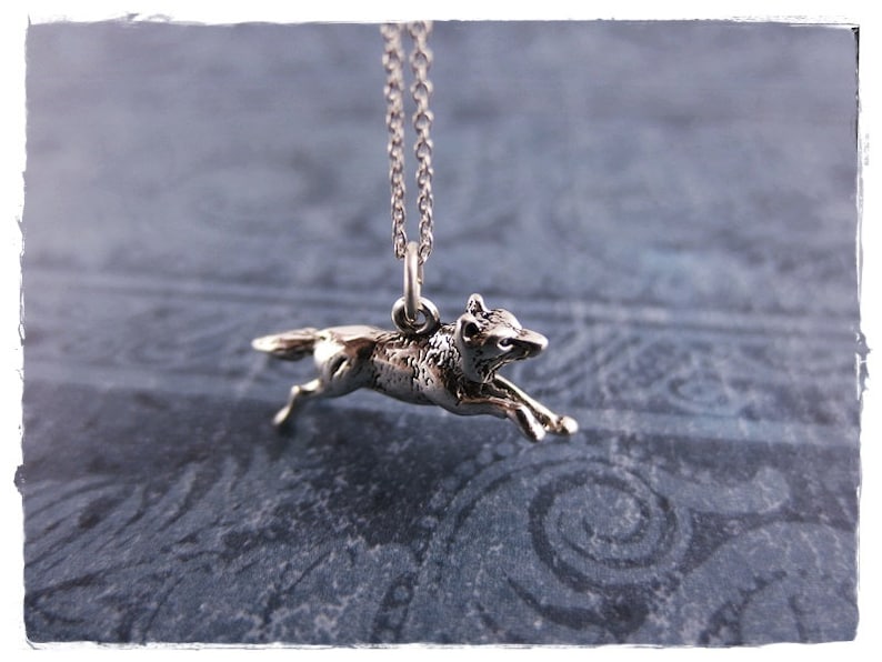 May include: A silver-toned pendant necklace featuring a running wolf charm. The wolf is detailed with textured fur and is suspended from a delicate chain. The pendant is approximately 1 inch in length, showcasing a wildlife theme.
