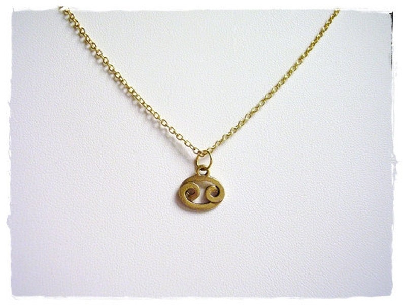 May include: A gold chain necklace with a small gold pendant in the shape of the Cancer zodiac sign.