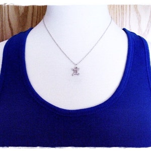 May include: A silver necklace with a small, silver pendant shaped like the letter 'I'. The necklace is on a white mannequin wearing a royal blue tank top.