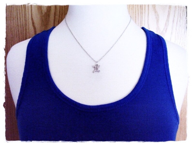 May include: A silver necklace with a small, silver pendant shaped like the letter 'I'. The necklace is on a white mannequin wearing a royal blue tank top.