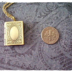 Peut inclure: Un collier avec un pendentif en forme de livre en or. Le pendentif a un design d&eacute;taill&eacute; et une petite ouverture ovale au centre.