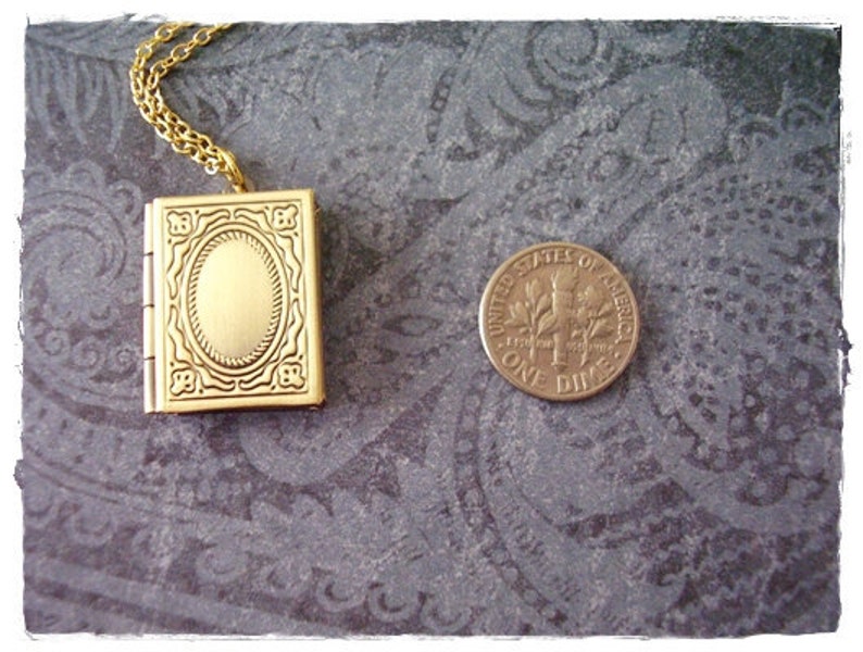Peut inclure: Un collier avec un pendentif en forme de livre en or. Le pendentif a un design d&eacute;taill&eacute; et une petite ouverture ovale au centre.