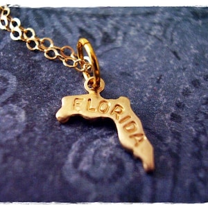 May include: Gold necklace with a pendant shaped like the state of Florida. The pendant has the word "FLORIDA" engraved on it.