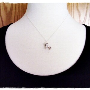 May include: A silver necklace with a small, detailed dog charm hanging from it. The necklace is on a white mannequin wearing a black tank top.