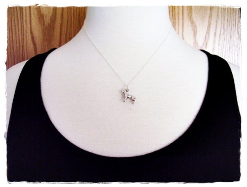 May include: A silver necklace with a small, detailed dog charm hanging from it. The necklace is on a white mannequin wearing a black tank top.