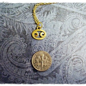 May include: Gold chain necklace with a gold Cancer zodiac sign pendant. The pendant is a stylized crab shape.